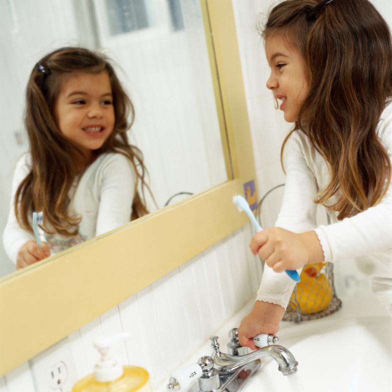 a baby girl holding her tooth brush and smiling in the mirror